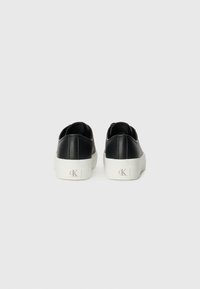 Black leather sneakers with a white rubber sole, featuring a low-cut design and subtle branding on the heel. Smooth texture.