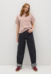 Camiseta rayada rosa y blanca, jeans oscuros de mezclilla con un corte relajado y puños enrollados, zapatillas rojas con detalles en beige; tela suave y corte holgado.