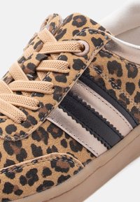 Gros plan sur une basket à imprimé léopard avec des lacets beige, des bandes latérales noires et beige, et une semelle en caoutchouc.