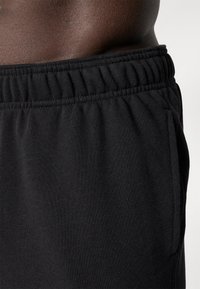 Black athletic shorts made of soft cotton blend; features elastic waistband, side pockets, and a textured fabric finish.