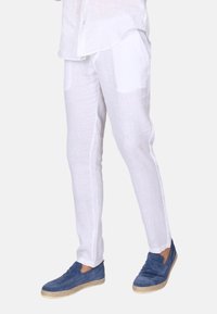 Bílé lněné kalhoty s úzkým střihem, se bočními kapsami a jemnou texturou. V kombinaci s modrými semišovými nazouvacími botami.