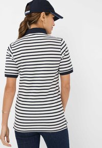 Polo a righe con strisce orizzontali blu navy e bianche, dotato di un colletto scuro, maniche corte e spacco laterale all'orlo.