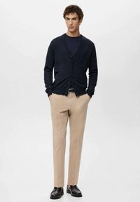 Granatowy sweter kardigan z guzikami i okrągłym dekoltem, zestawiony z jasnobeżowymi, dopasowanymi spodniami i czarnymi butami. Gładka faktura tkaniny, nowoczesny krój.