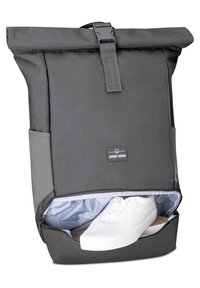 Gray roll-top backpack made of durable fabric, featuring a zippered compartment with white sneakers and a soft blue lining. Includes a logo tag.