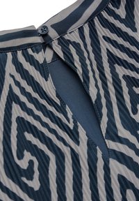 Prenda con un diseño en zigzag azul y beige, que cuenta con un cierre de botón y una abertura en la parte posterior. Tejido texturizado con rayas verticales.