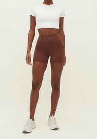 Ruskeat korkeavyötäröiset shortsit joustavasta materiaalista, yhdistettynä istuvaan valkoiseen crop-toppiin ja vaalean sävyisiin lenkkareihin. Sileä tekstuuri, minimaaliset saumat.