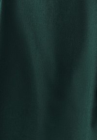 Grüner Stoff mit einer glatten Textur und subtiler Schattierung. Das Material wirkt atmungsaktiv und leicht, geeignet für Bekleidung oder Accessoires.