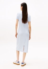 Light blue ribbed midi dress with short sleeves, back slit detail, and straight silhouette. Worn with white sneakers featuring blue accents.