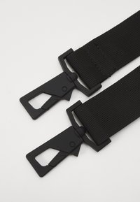 Sangle en nylon noir avec boucles en métal, présentant une surface texturée et un design robuste, sécurisée par des mécanismes ajustables à chaque extrémité.