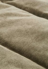 Texturiertes beiges Gewebe mit leichtem Glanz, das ein dezentes Rippmuster und eine weiche Oberfläche aufweist. Der Stoff fällt geschmeidig mit sichtbaren Falten.