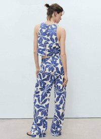 Twee-delig outfit bestaande uit een mouwloze top met een open rug en een pantalon met wijde pijpen. De stof vertoont een blauw bloemenpatroon op een crème achtergrond.