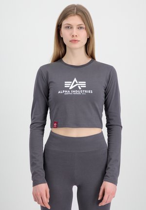 Grå cropped langærmet top med et hvidt logo, rund halsudskæring og synlig rød etiket; parret med matchende high-waisted leggings.