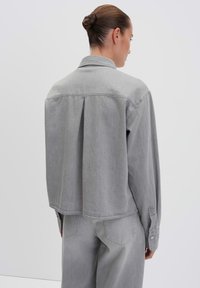 Gray denim shirt with a collar, long sleeves, and a relaxed fit. Features a back pleat and snap button cuffs.