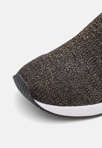 Chaussure de sport à motif noir et or, avec un dessus en tricot texturé et une semelle intermédiaire blanche contrastante avec une semelle extérieure noire texturée.