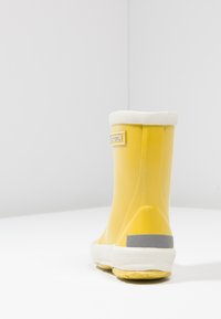Gele rubberen laars met een witte boord, grijze accenten op de hiel en een gestructureerde zool. Glad materiaal met een ronde vorm en merkdetail.