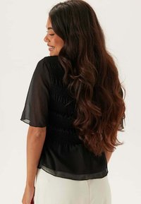 Sort bluse med smock-bag, gennemsigtige sommerfugleærmer og flydende design. Den har blød stof og en afslappet pasform.