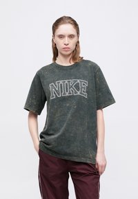 Veľká zelená tričko Nike s batikovaným vzorom, okrúhlym výstrihom a krátkymi rukávmi, s výrazným bielym nápisom naprieč hrudníkom.
