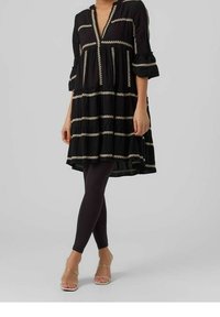 Black tunic dress with gold embroidery, V-neckline, and three-quarter sleeves; layered design with a longer back. Worn with black leggings.