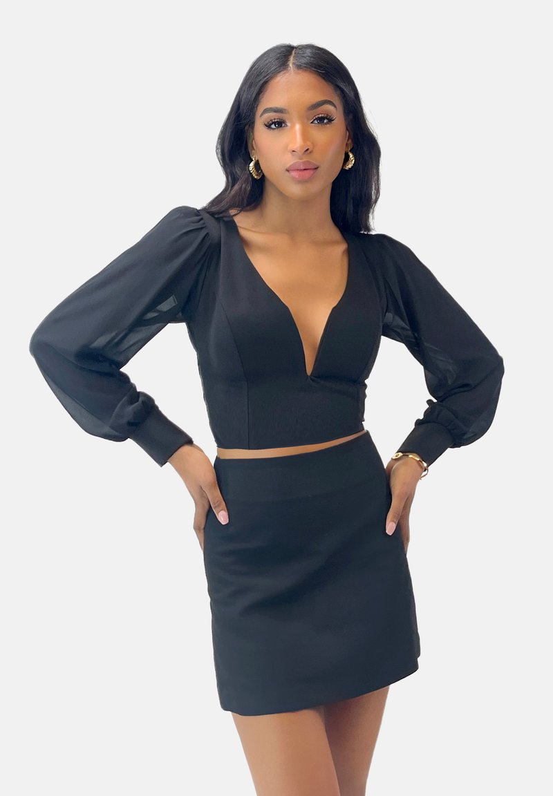 Zwarte crop top met diepe V-hals, pofmouwen en aansluitend lijfje, gecombineerd met een bijpassende zwarte minirok. Glad textuur, figuurvormend ontwerp.