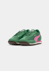Sneaker verde in suede e sintetico con una striscia laterale rosa, punta rotonda e suola testurizzata, con logo bianco e nero sulla linguetta.