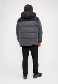 Puffjakke med en grå og sort farveskema, hætte, quiltet design og elastiske manchetter. Bæres med sorte bukser og sko.