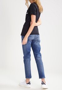 Camiseta de algodón negra combinada con jeans de mezclilla azul claro. El conjunto se completa con zapatillas blancas con acentos en azul marino.
