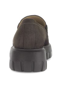 Donkerbruine suede schoen gezien van achteren, met een dikke, gekartelde zwarte rubberen zool en zichtbare stiksels op het midden van de hak.