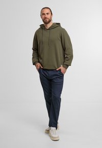 Olive green hoodie with adjustable drawstrings, paired with navy blue trousers and beige sneakers with light accents. Functional and casual design.