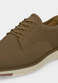 Baskets en tissu tricoté marron avec lacets et semelle blanche, gros plan sur l'avant et le côté de la chaussure.