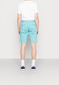 Shorts bleu clair à coupe décontractée, fabriqués en tissu lisse. Dotés de poches arrière et d'une taille, associés à des chaussettes blanches et des baskets.