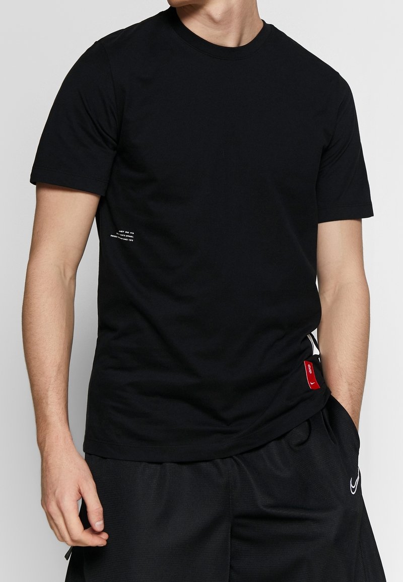 T-shirt en coton noir à manches courtes, col rond, petit détail de texte blanc sur le côté gauche, et un accent de label rouge à l'ourlet.