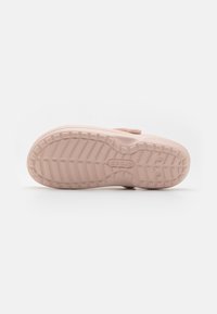 Semelle de chaussure en caoutchouc rose clair avec un motif текстурé, présentant des rainures pour l'adhérence et un logo circulaire au centre.