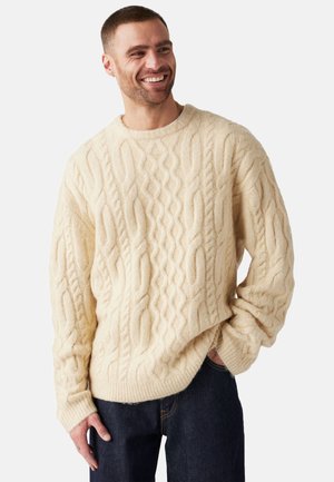 Beżowy sweter w splot kablowy z okrągłym dekoltem i ściągaczami, wykonany z miękkiej wełny, z teksturowanymi wzorami i luźnym krojem.