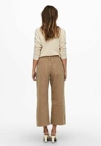 Pantalons beige à jambes larges en tissu texturé, dotés de poches arrière et d'une taille haute, associés à des talons ouverts.