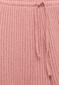 Ribbat rosa stickad tyg med dragsko i midjan. Mjuk textur med vertikala ränder som visar detaljer av öglor och stygn.