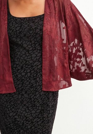 Kobieta nosząca przezroczysty bordowy kwiecisty kimono na czarnej, bezrękawnikowej sukience z abstrakcyjnym kamiennym wzorem.