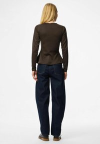 Långärmad, figursydd brun topp som är parat med löst sittande mörkblå jeans. Verkar slät med en lätt lystre, synliga sömmar och fickor.