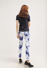 Černé tričko s krátkým rukávem, bílé kalhoty s modrým květinovým vzorem, slim fit, hladká textura a černé boty na klínku. Pohled ze zad.