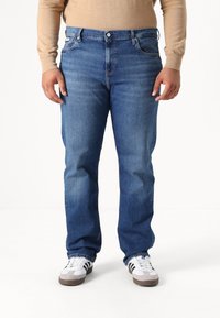 Jeans de mezclilla azul con un corte recto, diseño de cinco bolsillos y un ligero desgaste. Combinados con zapatillas blancas con franjas negras.