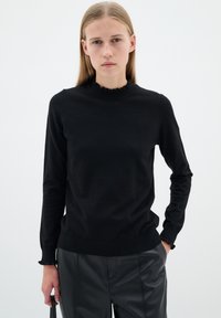 Svart långärmad tröja med en hög, volangformad hals. Tillverkad av ett glatt tyg, med en figursydd design och ribbade muddar och nederkant.