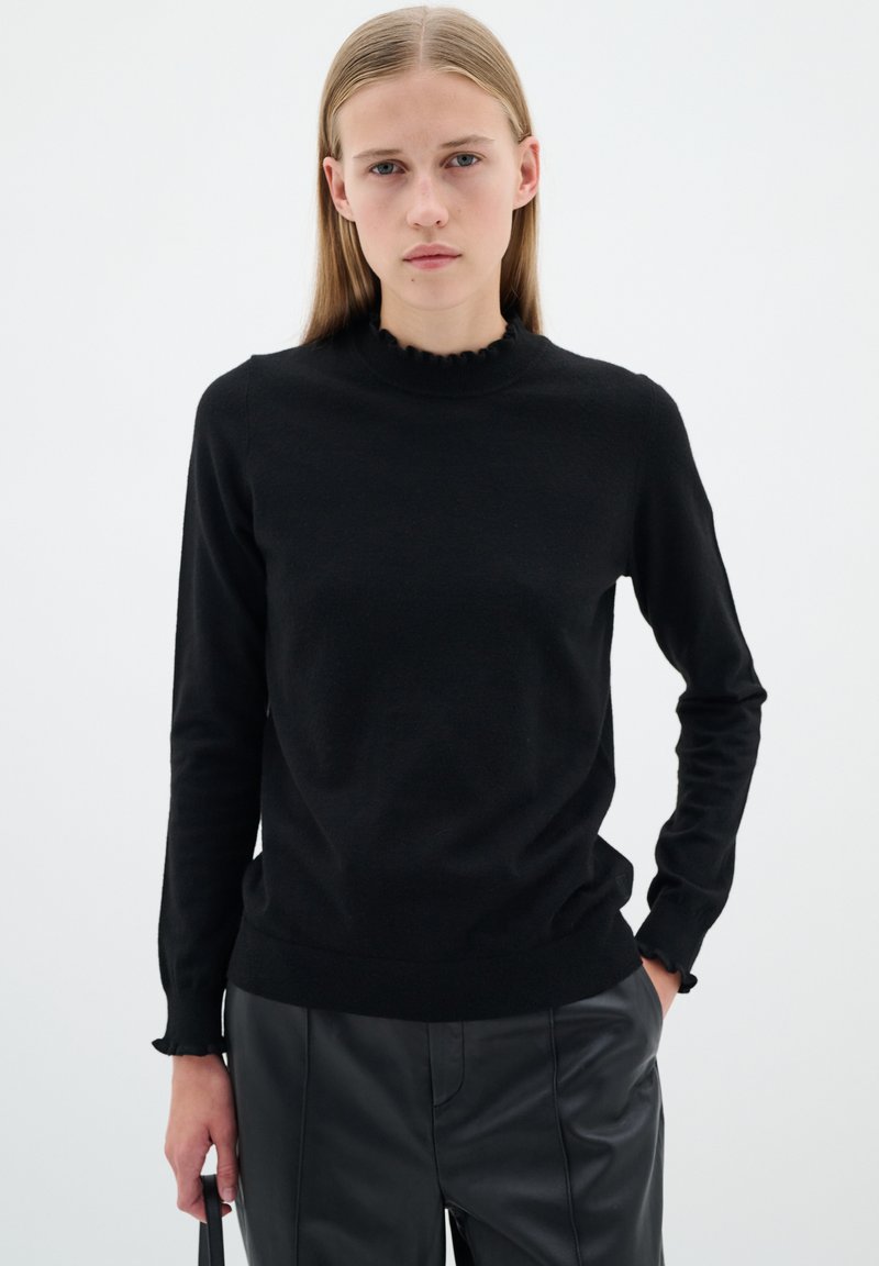 Svart långärmad tröja med en hög, volangformad hals. Tillverkad av ett glatt tyg, med en figursydd design och ribbade muddar och nederkant.