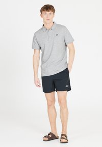 Grå kortärmad polo med krage, svarta sportshorts och bruna sandaler. Diskret logotypdetalj på skjortan och shortsen.