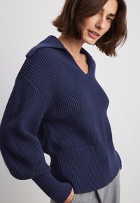 Navy blue knitted sweater with a v-neck and hood, featuring ribbed texture, wide sleeves, and a relaxed fit.