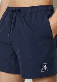 Pantaloni da bagno blu navy realizzati in tessuto leggero, dotati di una vita elastica con coulisse e tasche laterali. Include un dettaglio con il logo del marchio.