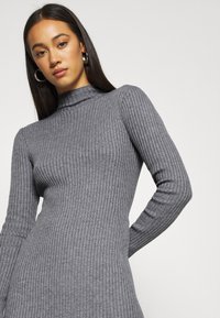 Graues geripptes Langarmkleid mit hohem Kragen. Die Stofftextur ist weich, das taillierte Design betont die Silhouette.