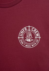 Bordo crewneck majica od bombaža, z belim krožnim logotipom, ki vsebuje besedilo "UNFR CREW" in "DON'T MESS WITH US". Gladka tekstura.
