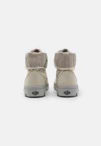 Beige canvas ankle boots with a gray sole and a folded cuff. Features a round logo on the side and a textured tread pattern for grip.
