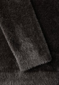 Czarna, włochata tkanina o miękkiej, teksturowanej powierzchni, z różnymi odcieniami ciemnoszarego i puszystym wykończeniem, z dwoma zachodzącymi na siebie sekcjami.