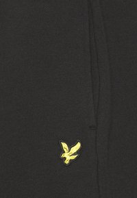 Tissu de sweat-shirt noir avec texture côtelée. Présente un petit logo d'aigle jaune brodé sur le bas à gauche.