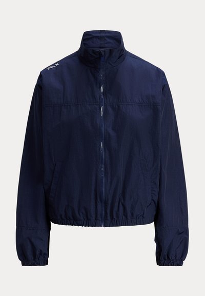 Marineblå vindjakke med høy krage, glidelås foran, elastiske mansjetter og sidelommer. Lett, teksturert stoff.